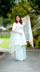 Smiling Indian woman in elegant saree posing outdoors on a sunny day.