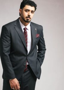 Confident man in grey suit with red tie against neutral backdrop.