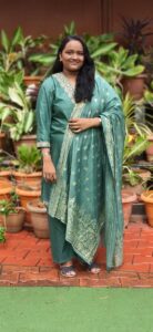 Woman in green traditional dress standing among potted plants outdoors.