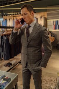 Businessman in tailored gray suit using smartphone in a clothing boutique.