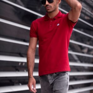 A fashionable man in a red polo shirt and sunglasses walks confidently outdoors.