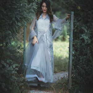 A graceful woman in a blue dress walking through a lush outdoor setting in Kashmir.