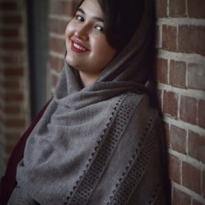 a woman wearing a shawl standing next to a brick wall