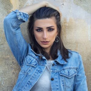 woman in blue denim button up jacket leaning on brown wall