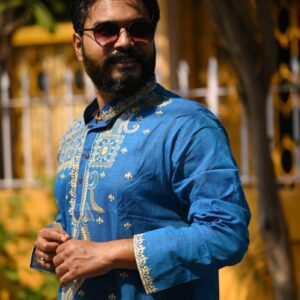 Man in blue kurta with sunglasses poses outdoors.